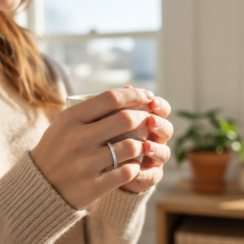 Bee-Bees 2mm D color moissanite eternity band in sterling silver worn on a finger while holding a warm mug
