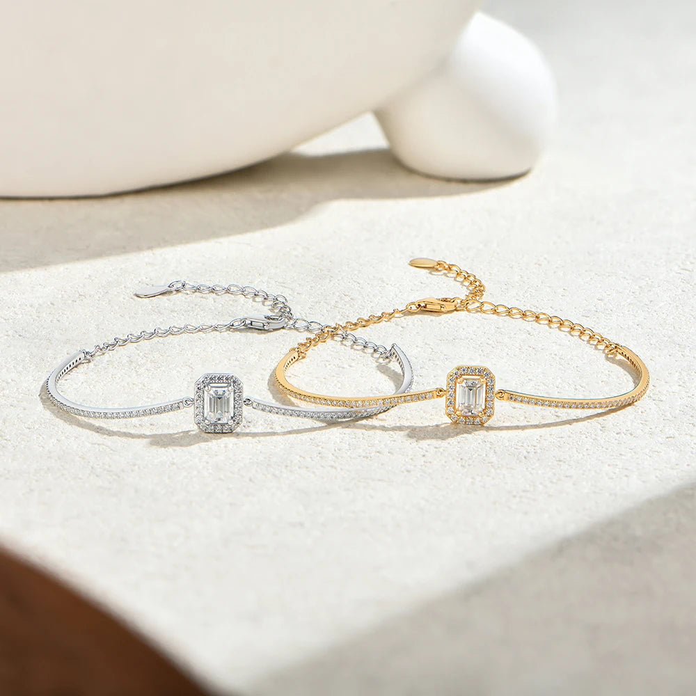 Bee-Bees emerald cut moissanite tennis bracelets in silver and gold plated sterling silver on a textured surface.