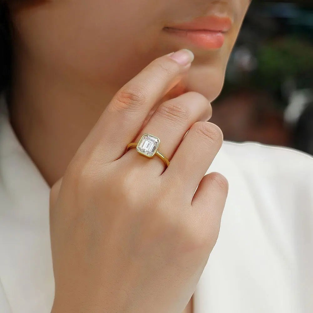 Bee-Bees 2CT emerald cut moissanite engagement ring in 18k white gold plated sterling silver with a bezel setting.