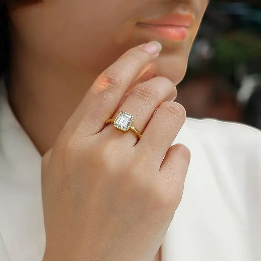 Bee-Bees 2CT emerald cut moissanite engagement ring in 18k white gold plated sterling silver with a bezel setting.