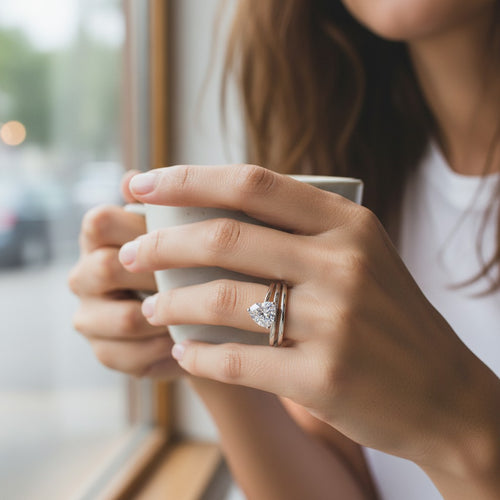 Bee-Bees 1ct heart cut moissanite spiral eternity ring in sterling silver worn on a woman's finger holding a mug