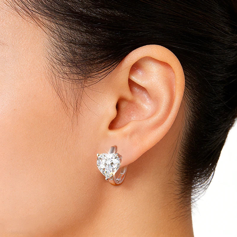 Bee-Bees 1CT heart-cut moissanite huggie hoop earrings in 925 sterling silver worn on a woman's ear