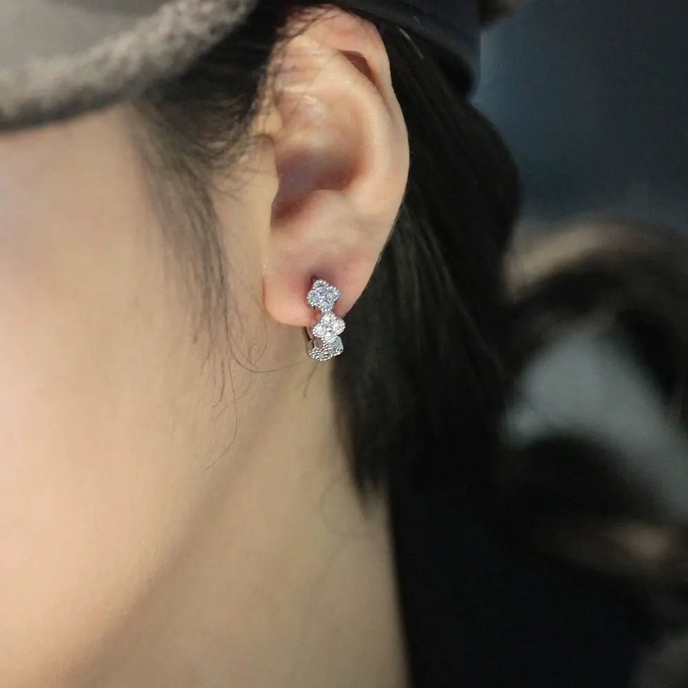 Bee-Bees four leaf clover huggie earrings in sterling silver with sparkling D color moissanite stones on an earlobe