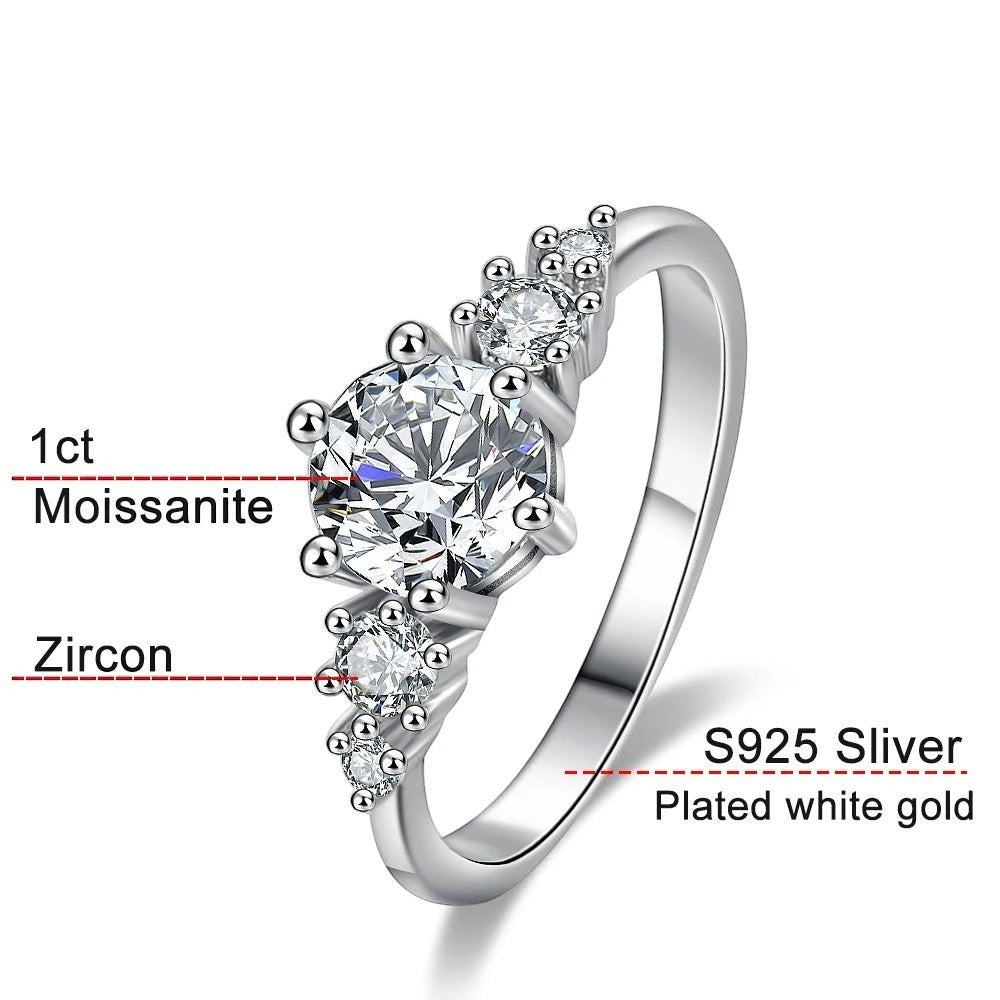 Bee-Bees 1ct round Moissanite engagement ring in s925 sterling silver with 18k white gold plating. Features a solitaire stone with smaller accent stones.