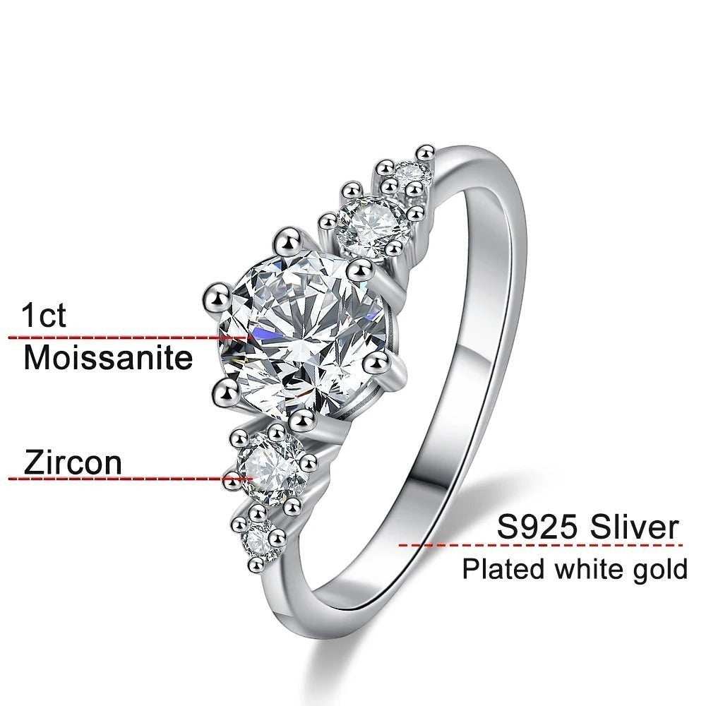 Bee-Bees 1ct round Moissanite engagement ring in s925 sterling silver with 18k white gold plating. Features a solitaire stone with smaller accent stones.