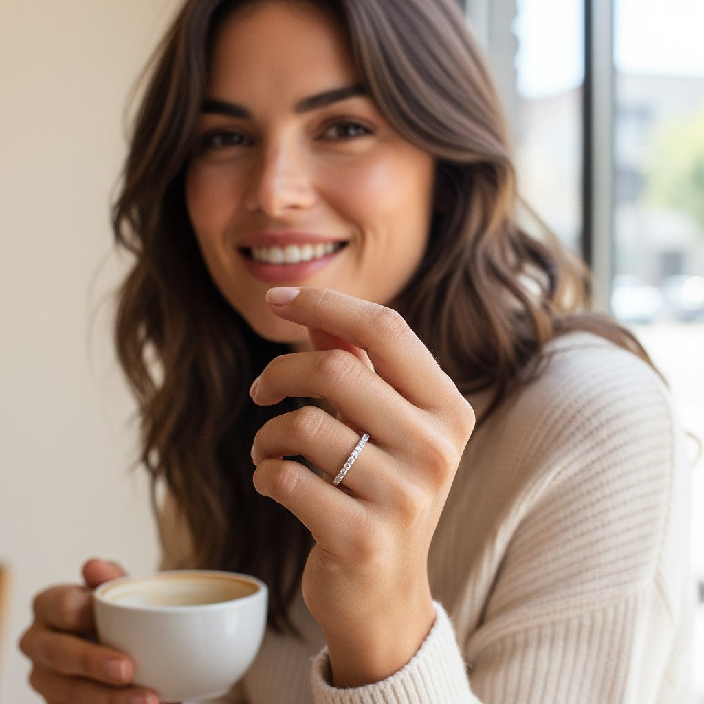 A woman wearing a Bee-Bees 2mm D color moissanite eternity band in sterling silver while holding a coffee cup.