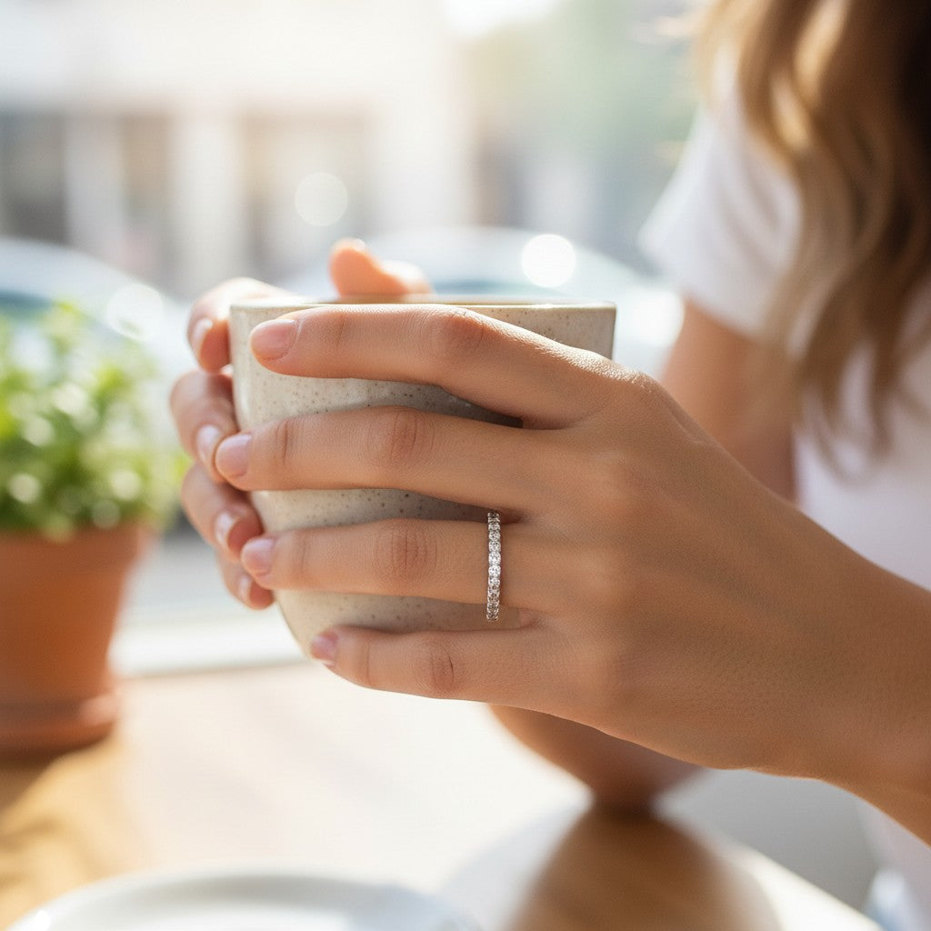 Bee-Bees 2mm D color moissanite eternity band in sterling silver worn on a woman's finger while holding a coffee mug