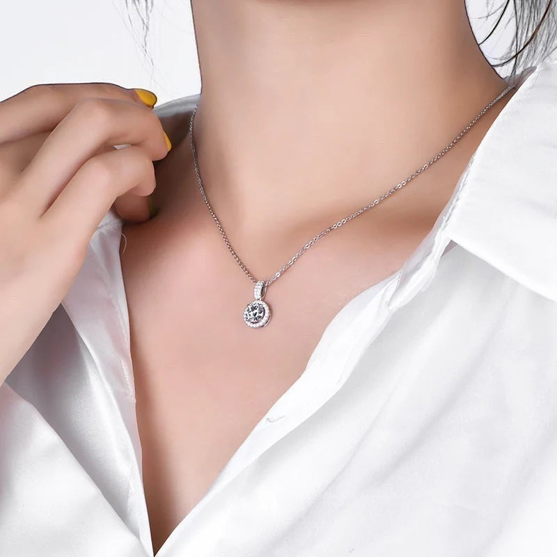 Bee-Bees solitaire Moissanite necklace with round-cut center stone and halo, on a silver chain, worn by a woman.