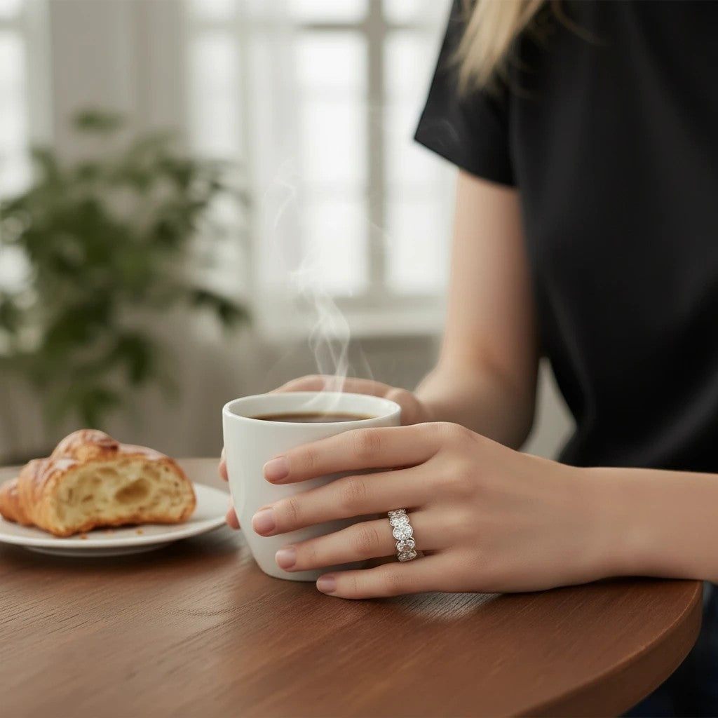 Bee-Bees 0.5ct oval moissanite eternity ring in 18k white gold plated silver worn on a hand holding a coffee mug.