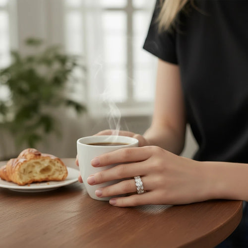 Bee-Bees 0.5ct oval moissanite eternity ring in 18k white gold plated silver worn on a hand holding a coffee mug.