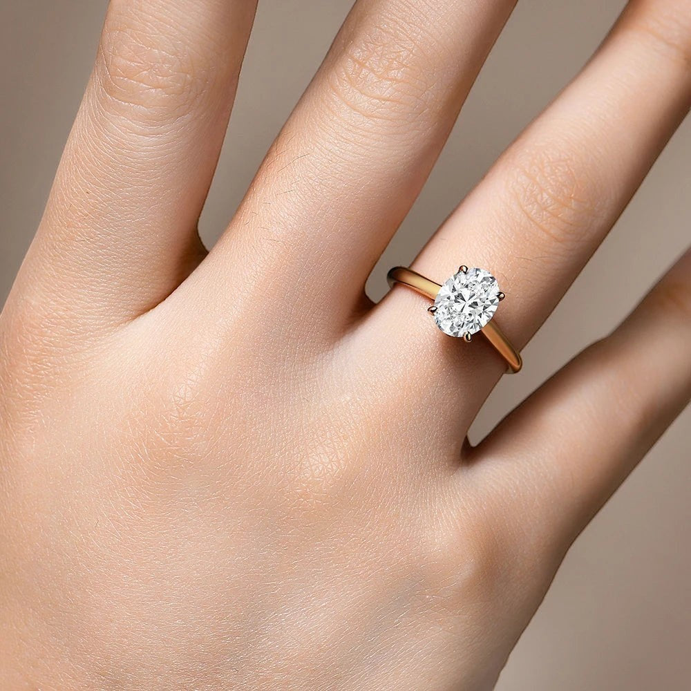 Bee-Bees 2CT oval-cut moissanite engagement ring with a classic four-prong setting on a gold band worn on a finger.