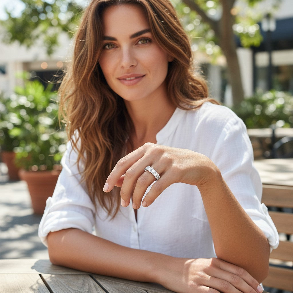 Bee-Bees princess cut moissanite wedding band in 18k gold-plated sterling silver worn by a woman at an outdoor cafe.