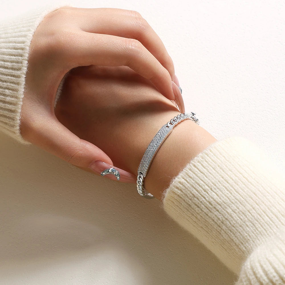 Bee-Bees sterling silver Cuban link bangle featuring sparkling D color VVS1 moissanite stones on a woman's wrist.