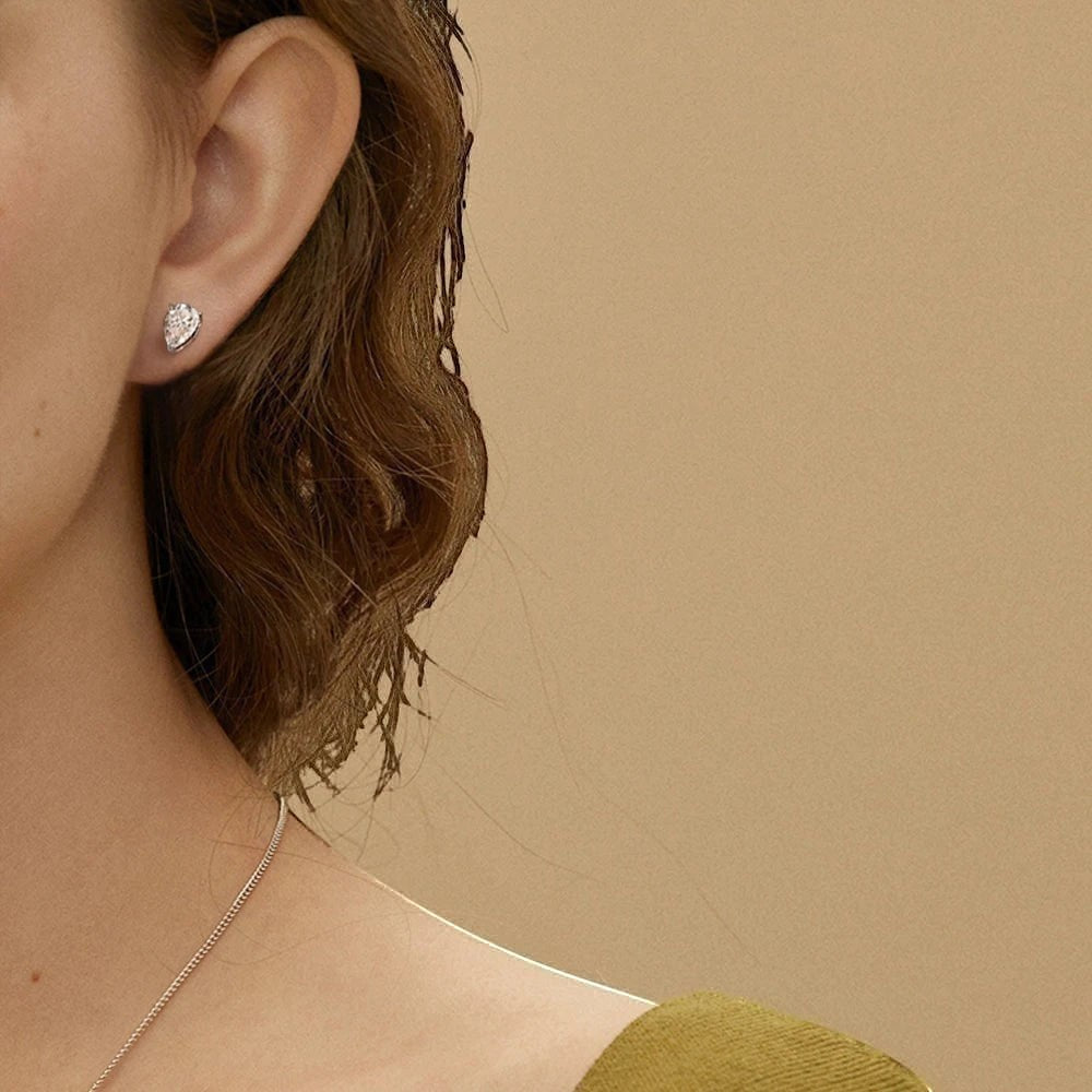D color VVS1 pear cut moissanite stud earrings in a 925 sterling silver setting worn on a model's earlobe.