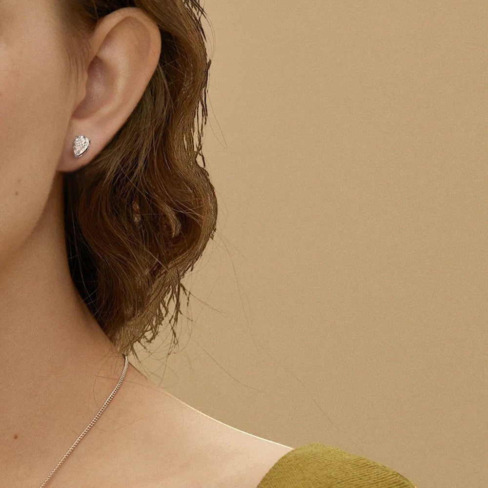 D color VVS1 pear cut moissanite stud earrings in a 925 sterling silver setting worn on a model's earlobe.